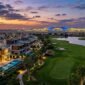 Luxury modern villas overlooking golf course with illuminated Al Maktoum Airport mega-terminal at dusk