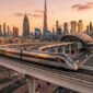 Modern aerodynamic Etihad Rail passenger train on elevated track overlooking Dubai skyline and multi-modal transit station at sunset