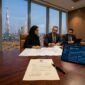 Institutional executive boardroom in DIFC with real estate acquisition legal contracts, architectural blueprints and Burj Khalifa skyline view
